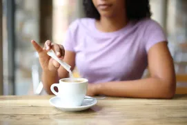 Mujer añadiendo azúcar al café.