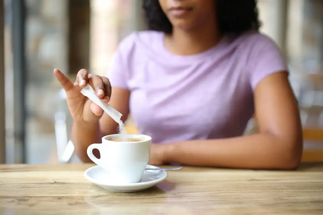 Mujer añadiendo azúcar al café.